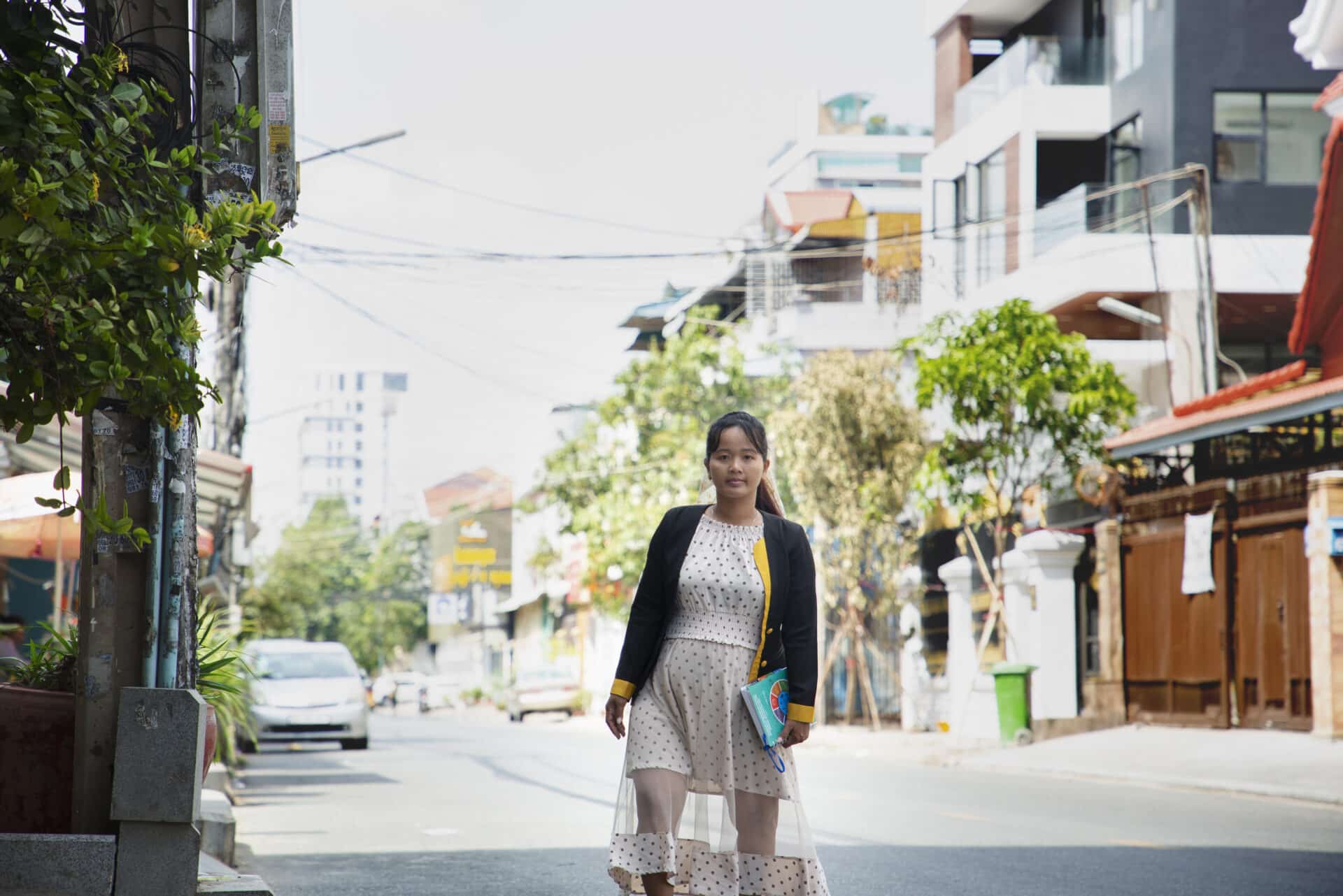 Sokhak is wearing a light dress and standing in a street.