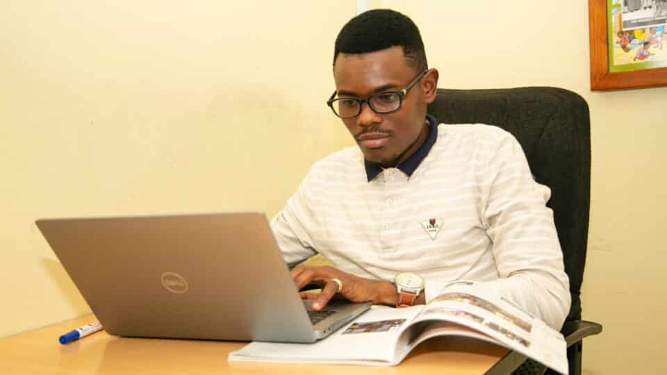 Daniel a Tanzanian young leader sits working at his laptop.